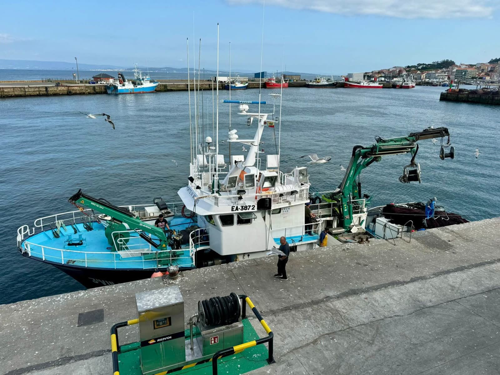 Barco do porto de Aguiño atracado no peirao coa tripulación preparando as redes