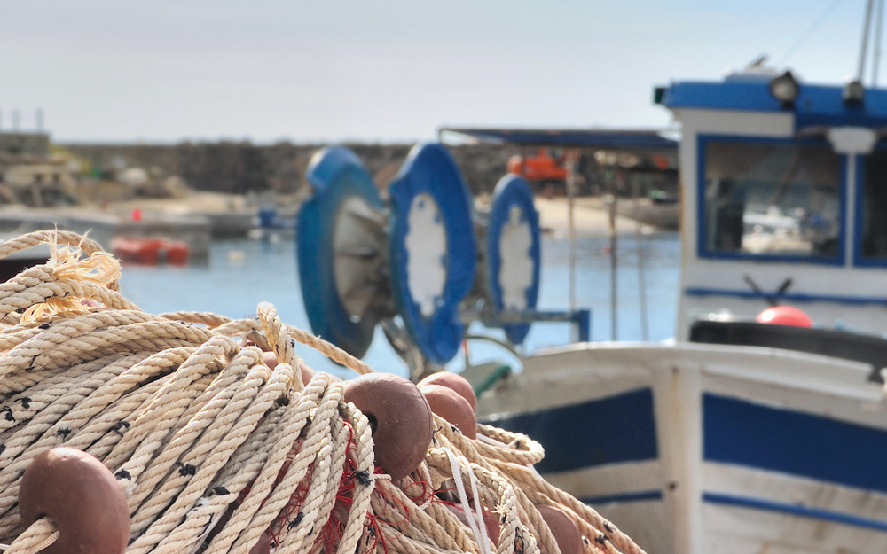 Cabos e aparellos de pesca sobre o peirao, cun barco de litoral ao fondo