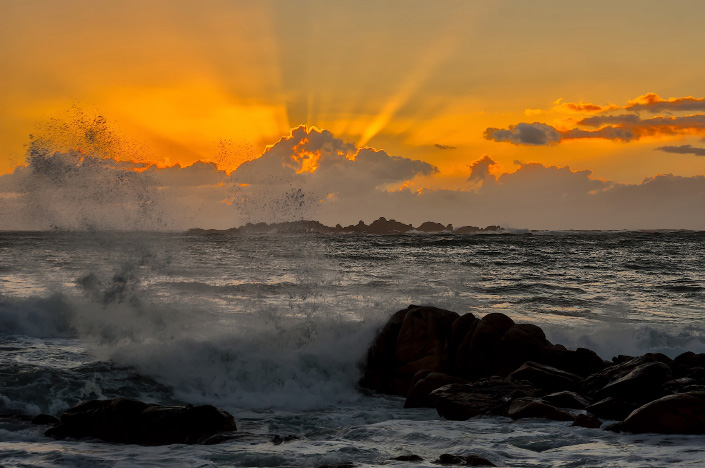 Solpor con raios de luz sobre a illa de Sagres e o mar rompendo nas rochas