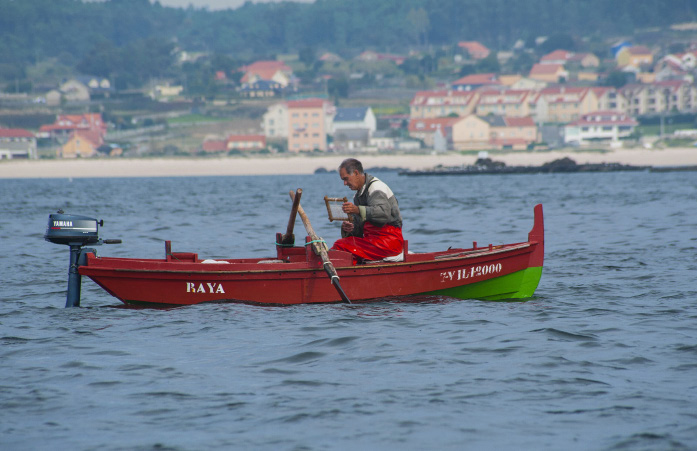Mariñeiro pescando polbo nunha gamela vermella fronte á praia do Castro